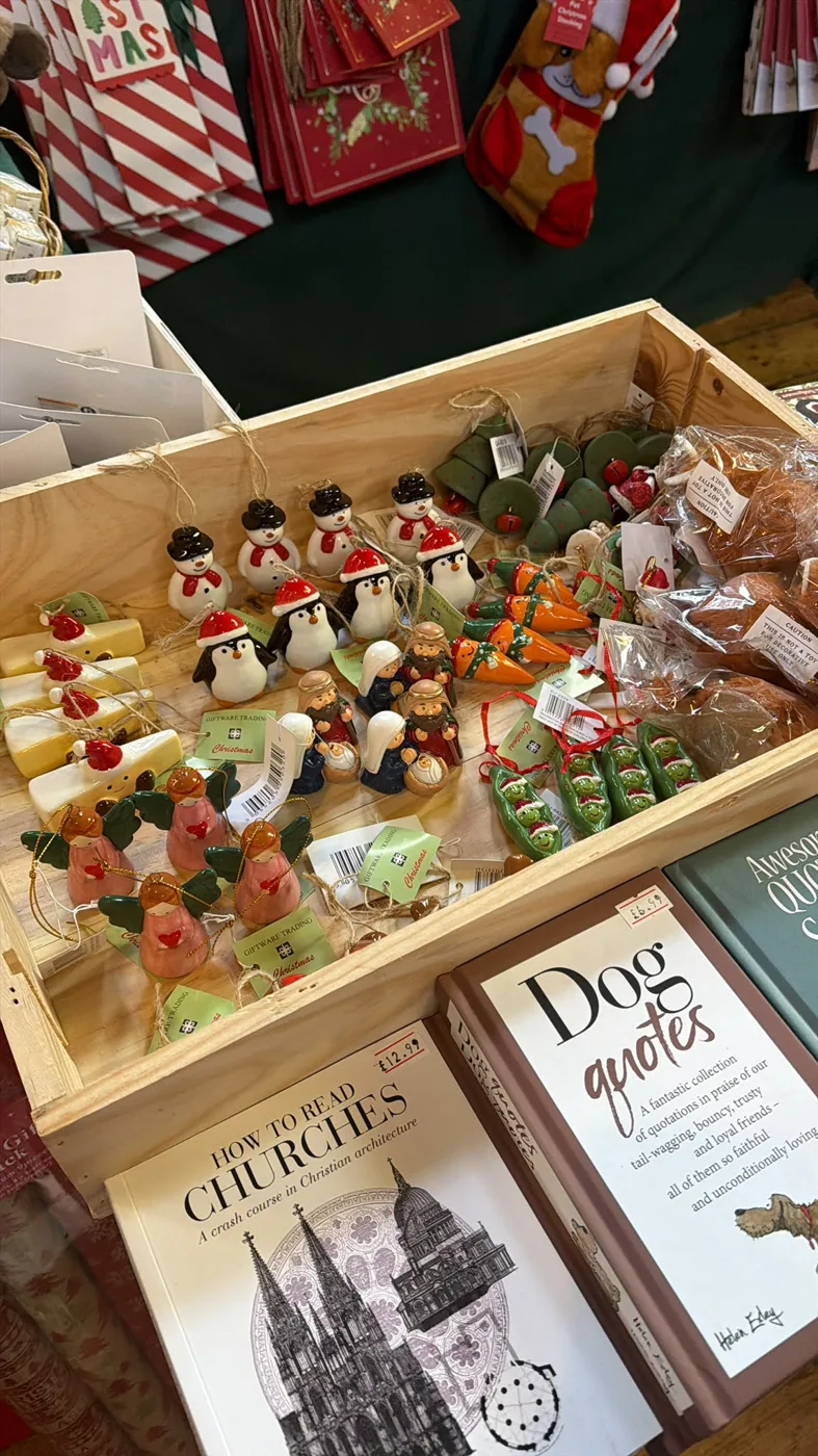 A wooden crate of small Christmas tree decorations, including penguins, robins and carrots, with books in front and boxed Christmas cards behind