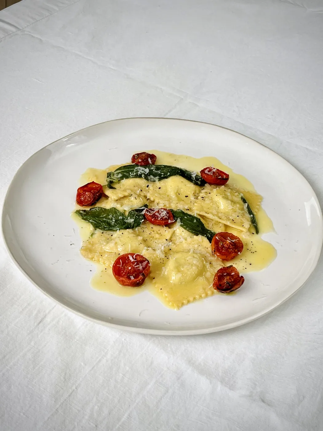 Square ravioli in a butter sauce with sage leaves and roasted cherry tomatoes on a white plate