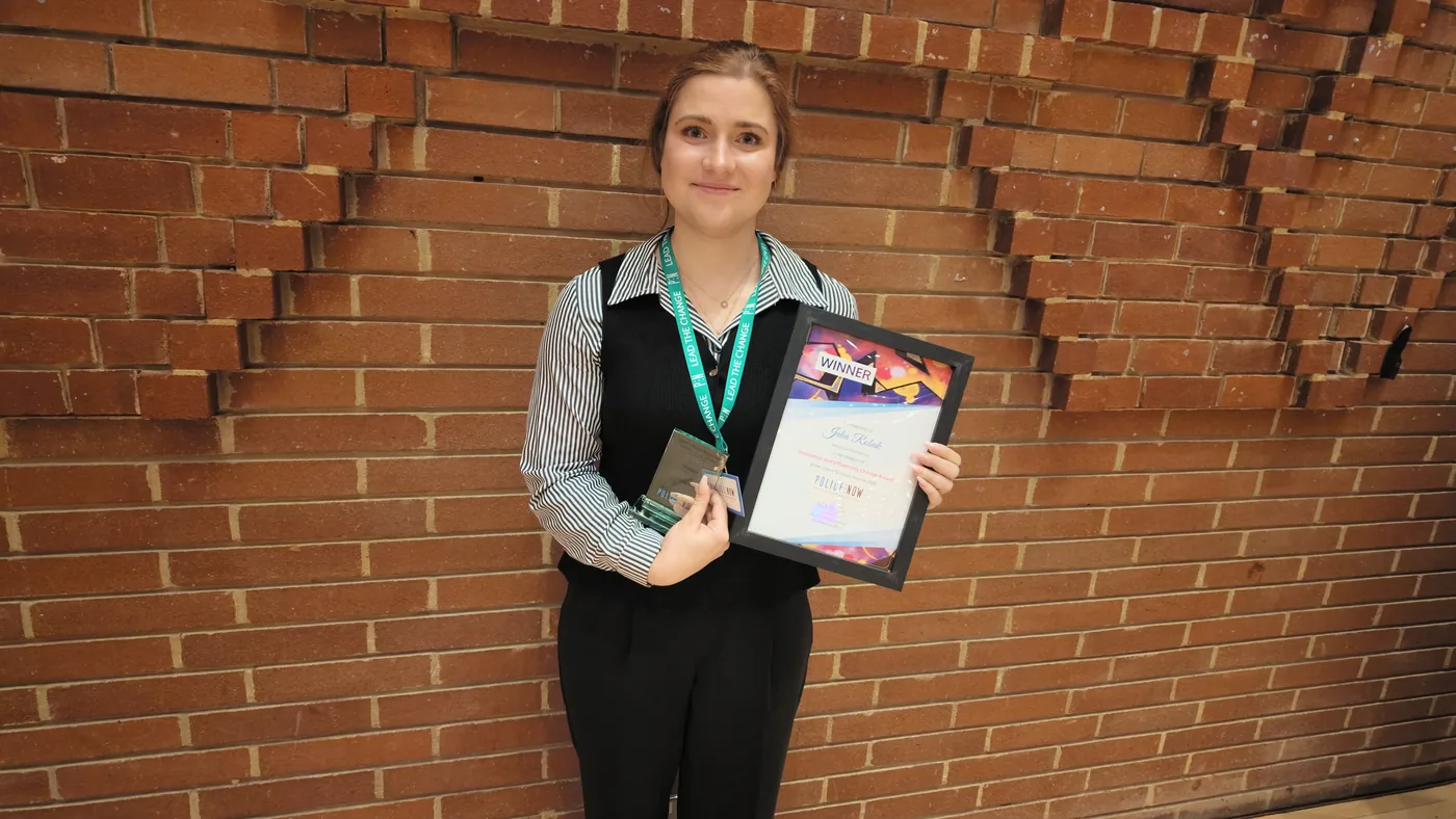 PC Julia Robak holding her trophy and framed winner's certificate against a brick wall