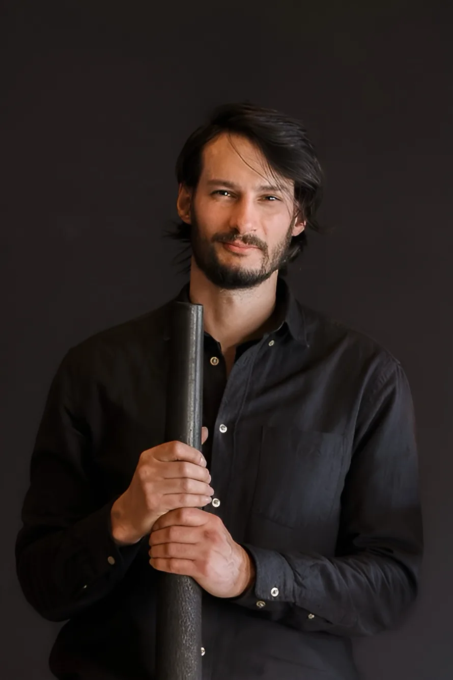 Christian Dimarco holding a didjeridu against a dark background