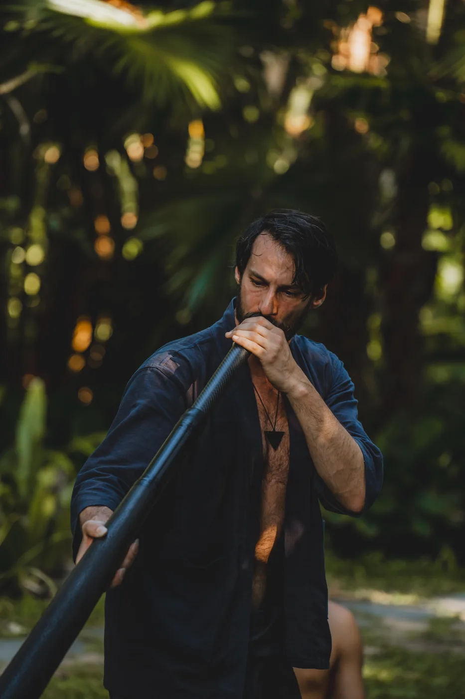 Christian Dimarco playing a didjeridu among tropical plants