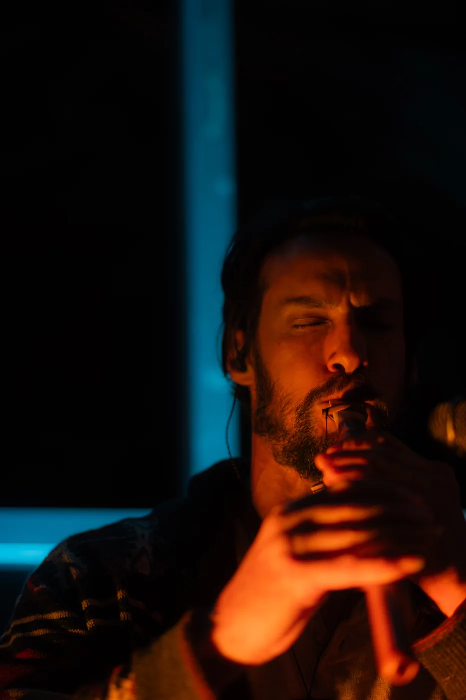 Christian Dimarco playing a small wooden wind instrument with his eyes closed, lit in orange