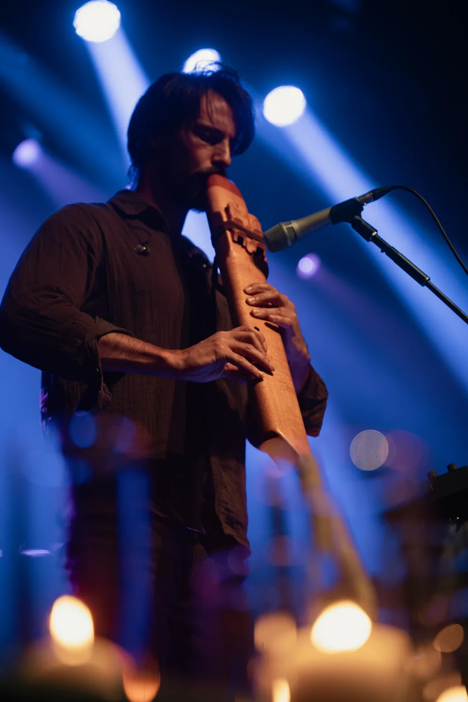 Christian Dimarco playing a wooden flute into a microphone under blue stage lights