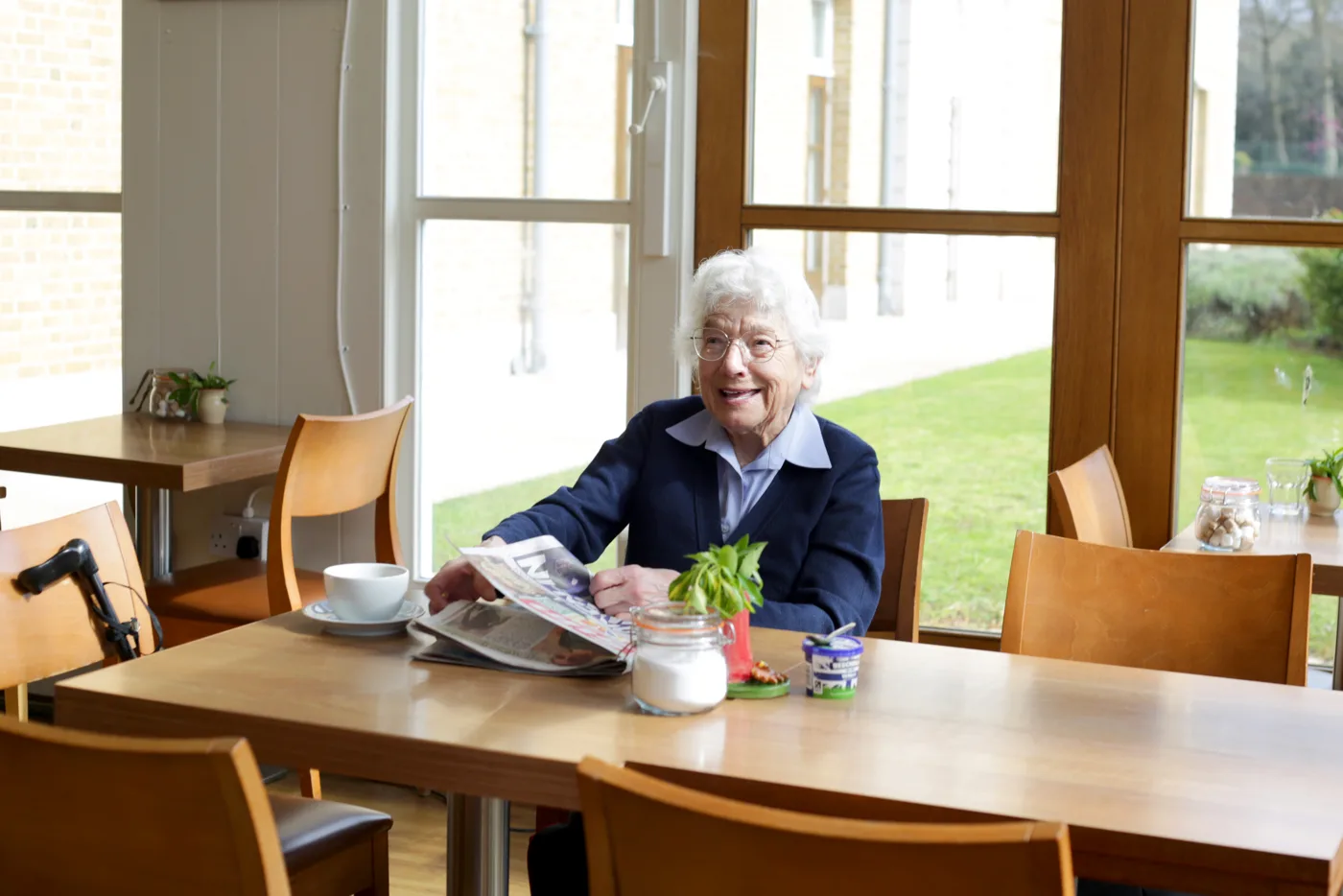 A Chelsea Pensioner with her newspaper and a cup of tea at a café table