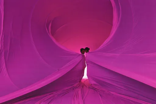 Two performers standing inside billowing folds of bright pink fabric