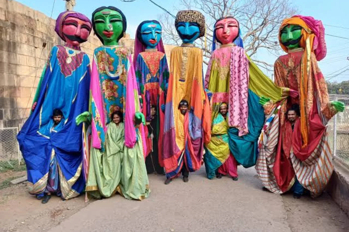 Six giant puppets in brightly coloured robes with large painted faces, with their puppeteers visible underneath